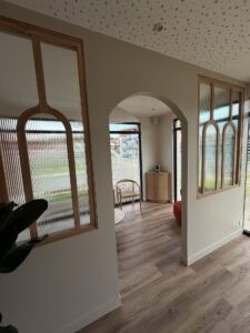 Intérieur moderne. Pièce lumineuse avec arches, panneaux bois et verre cannelé. Plafond texturé, sol parquet clair. Design contemporain épuré.