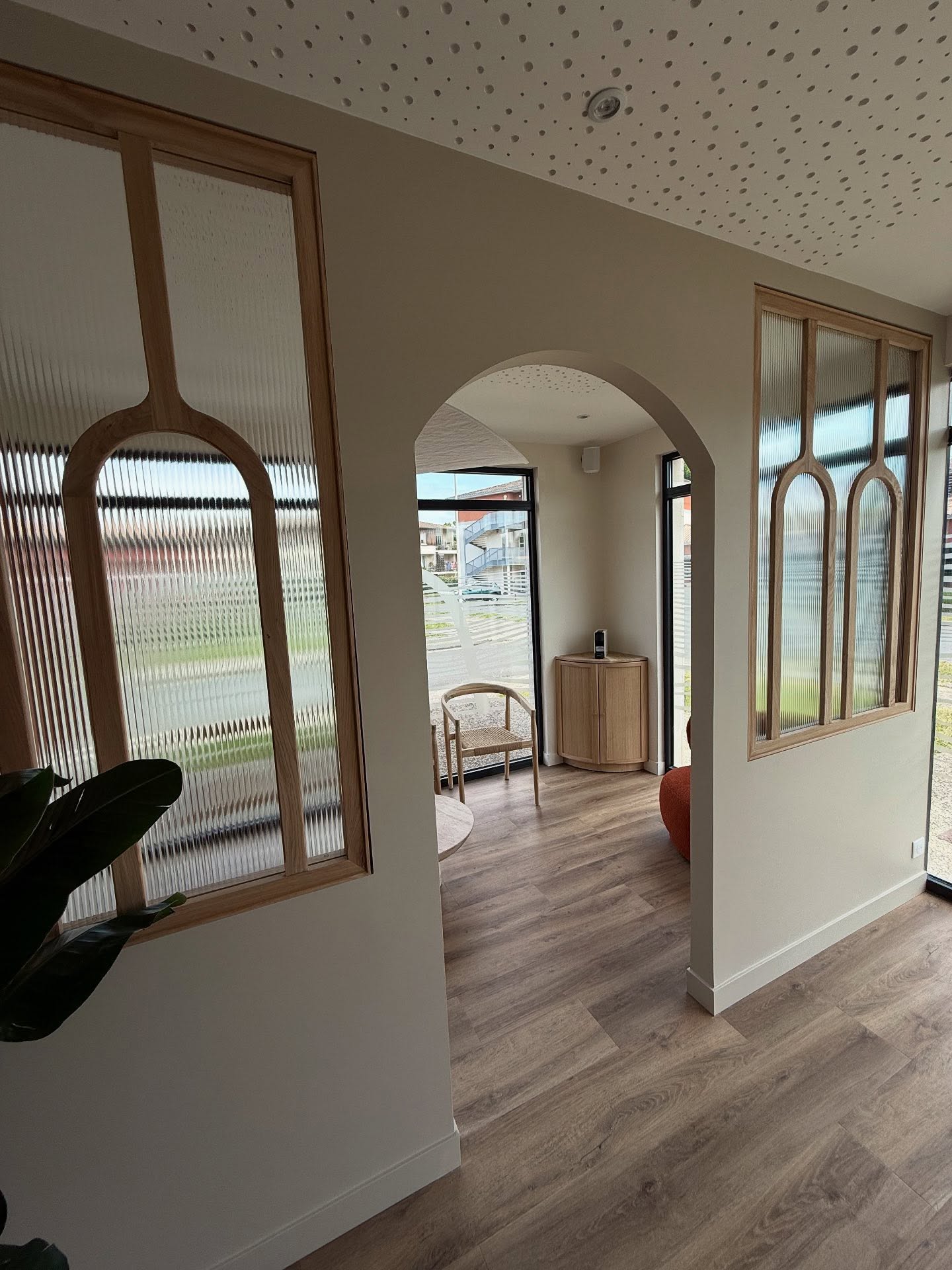 Intérieur moderne. Pièce lumineuse avec arches, panneaux bois et verre cannelé. Plafond texturé, sol parquet clair. Design contemporain épuré.