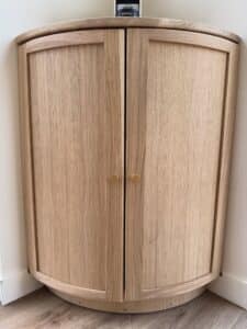 Meuble d'angle sur mesure en bois clair avec deux portes et poignées dorées. Un appareil KRUPS Nespresso est posé sur le dessus.