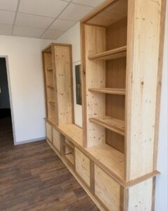 Meuble de rangement modulaire en bois clair avec étagères et placards. Design sur mesure dans une pièce moderne avec murs blancs et sol stratifié.