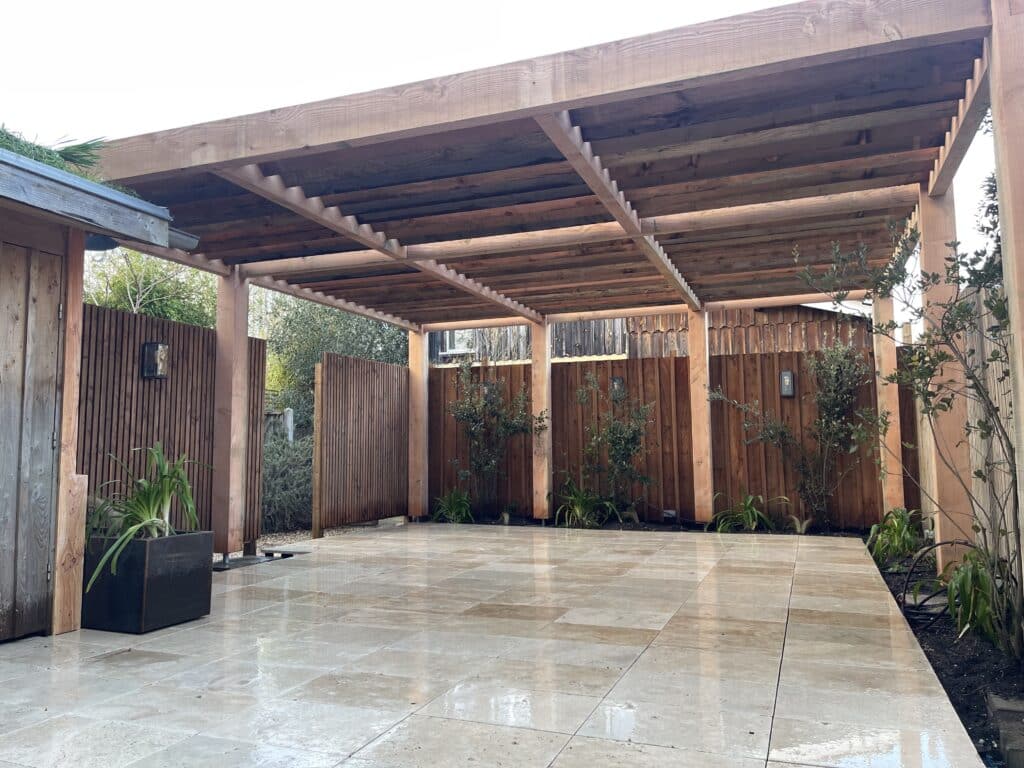Pergola Bois Moderne & Terrasse Carrelée Lumineuse Pergola en bois clair au-dessus d'une terrasse carrelée beige brillante. Clôtures en bois foncé, plantes vertes et lumières murales. Espace extérieur moderne.