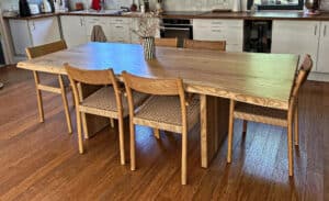 Table à manger en bois clair live edge avec six chaises en bois et rotin dans une cuisine moderne. Vase rayé avec fleurs sur la table.