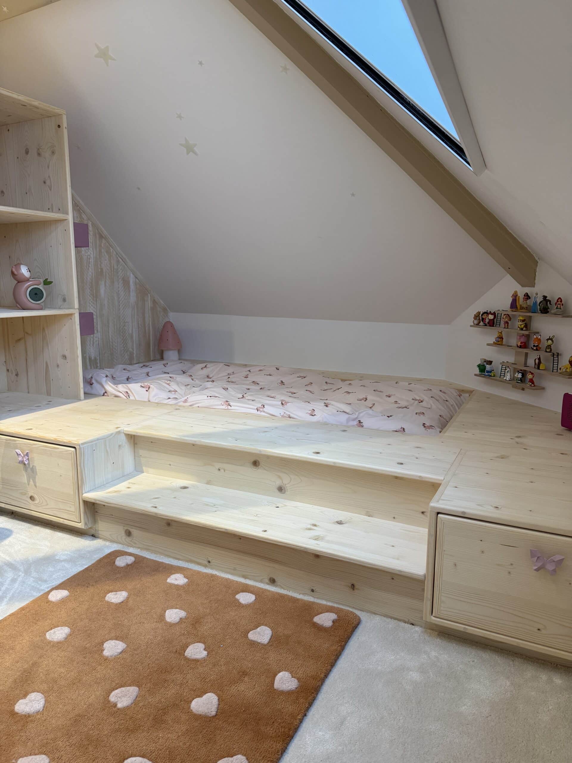 Chambre mansardée bois clair. Lit plateforme à tiroirs, escalier, lucarne. Murs étoilés et jouets sur étagères murales.