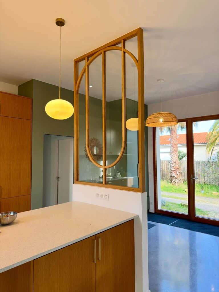 Cuisine moderne avec verrière en arche et îlot en bois Cuisine moderne avec îlot, verrière en arche boisée, mur vert sauge et suspensions design.